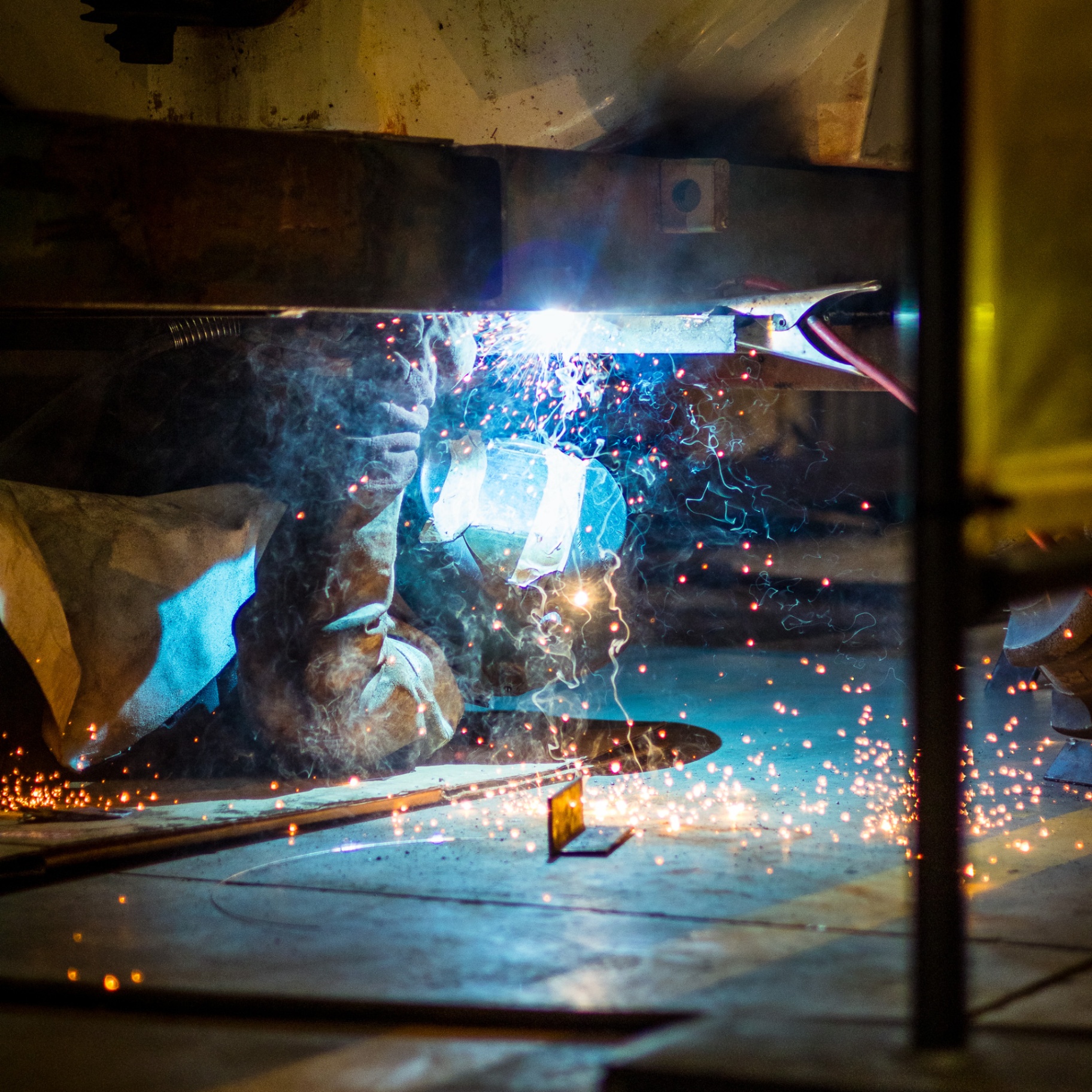 Welder working underneath a tank with bright arc and sparks
