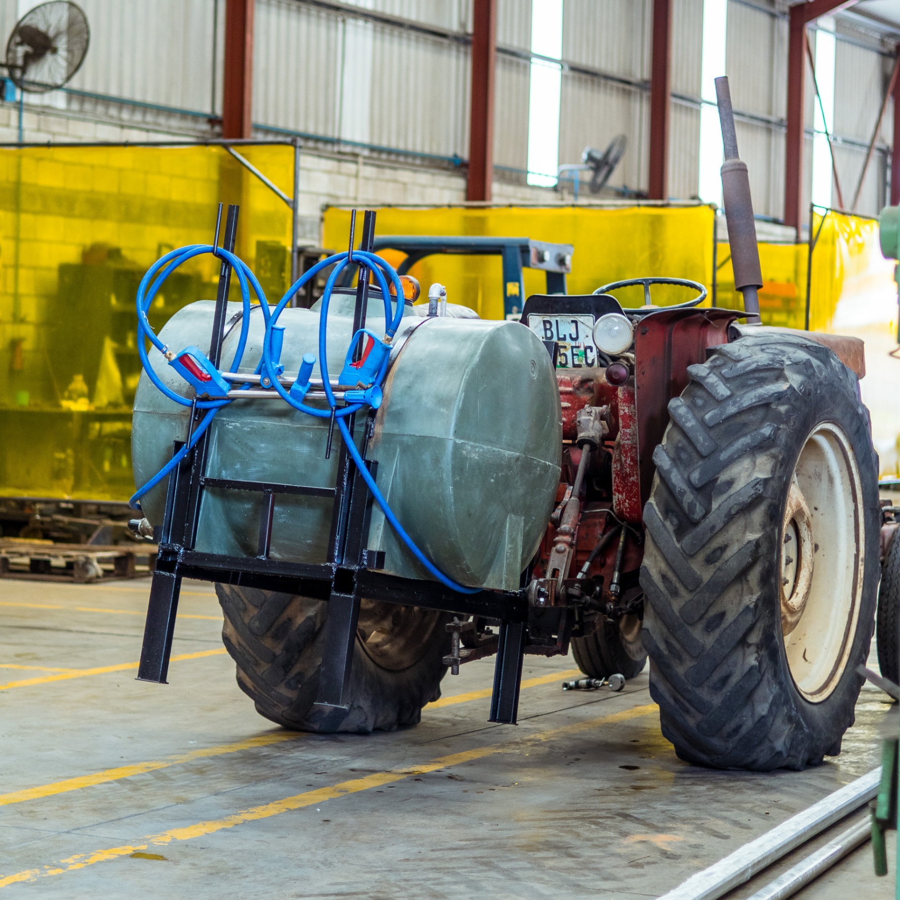 Vintage red tractor fitted with a mounted spray tank and blue hose reels