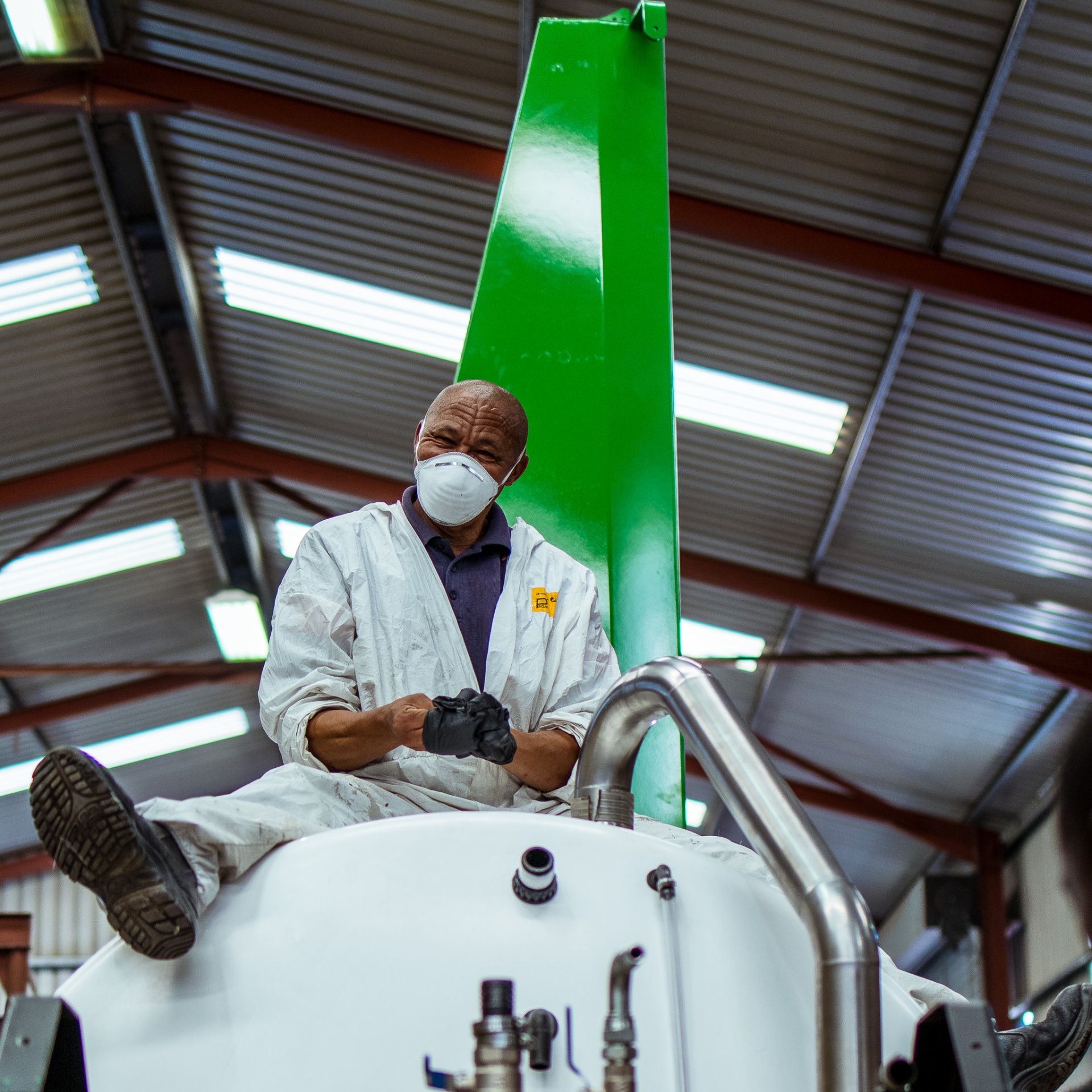 Turn-Rite paint technician in protective suit working on top of a green and white HelixSpray unit
