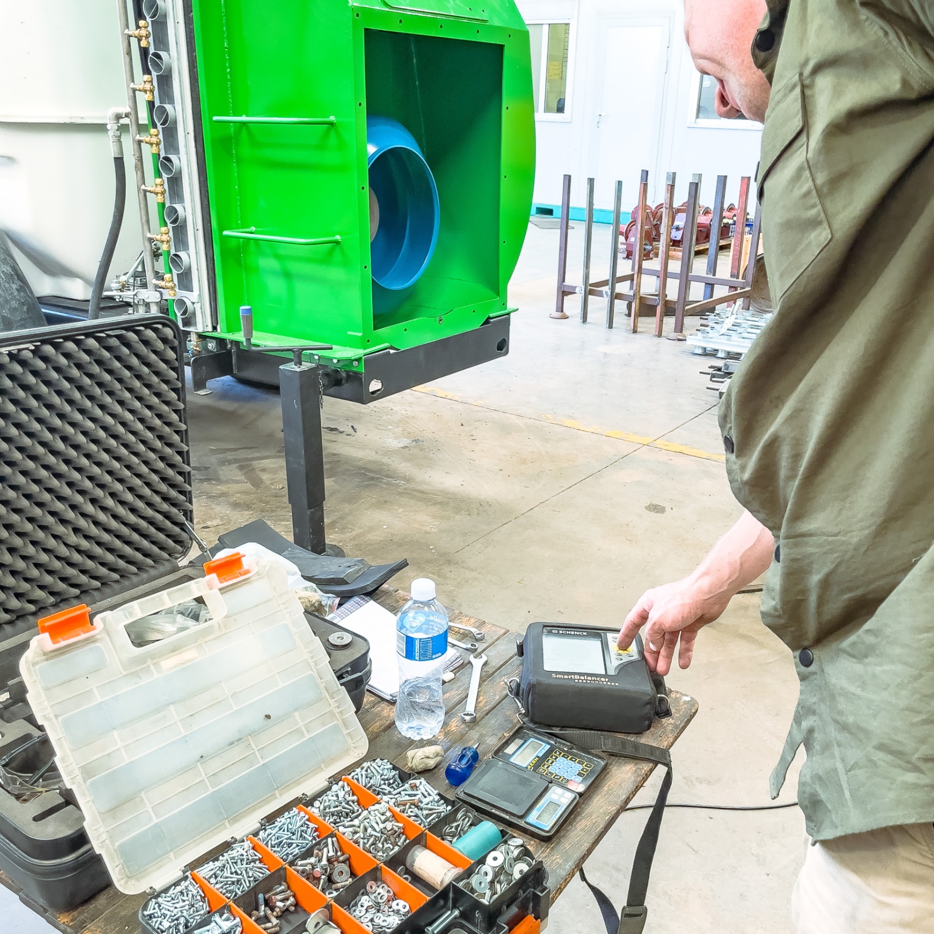 Technician calibrating balancing equipment beside a green spray machine in the workshop