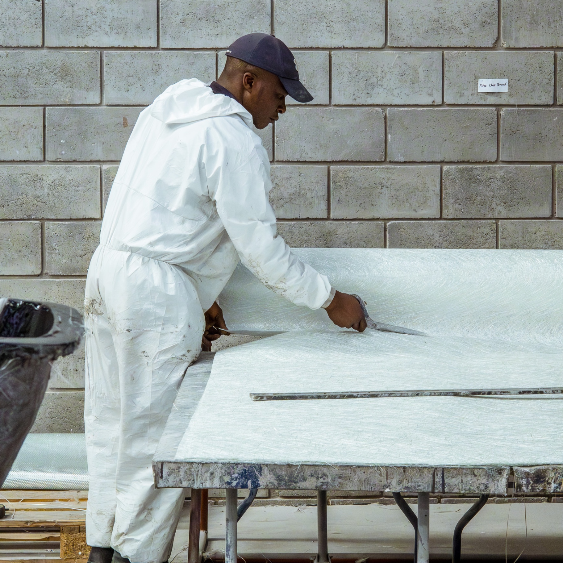 Worker in protective overalls cutting fibreglass material on a large table