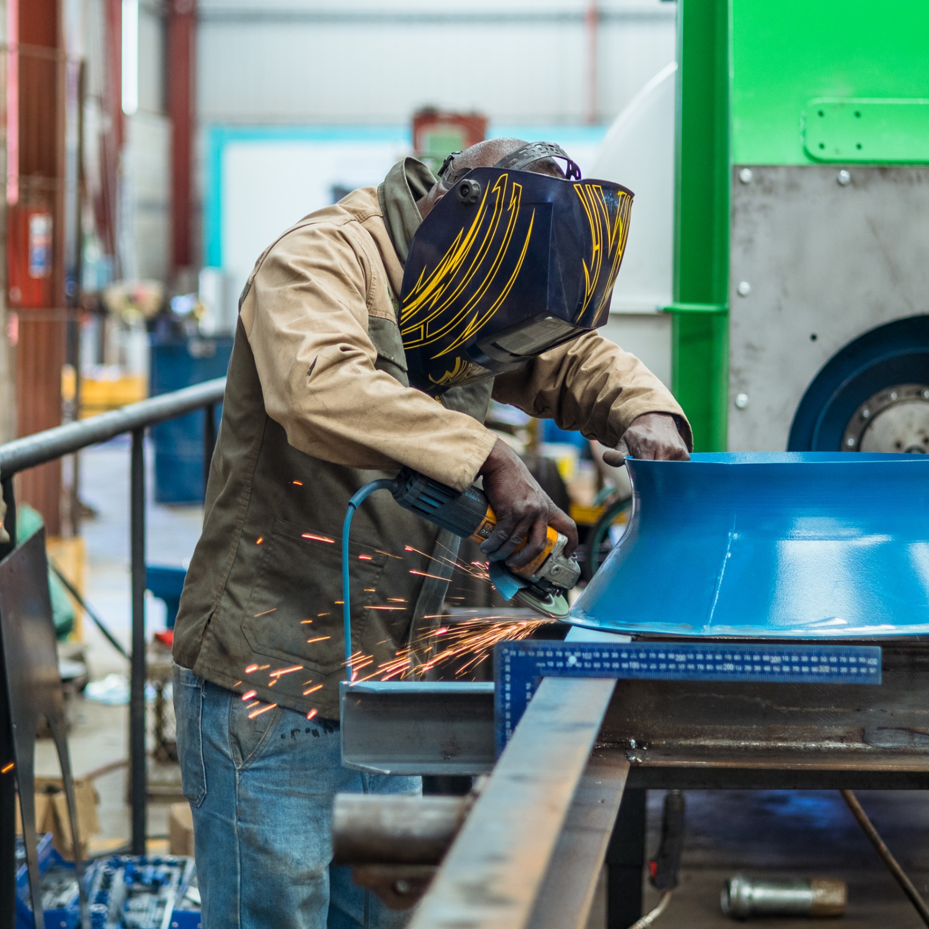 Workshop technician grinding a blue metal component with sparks flying